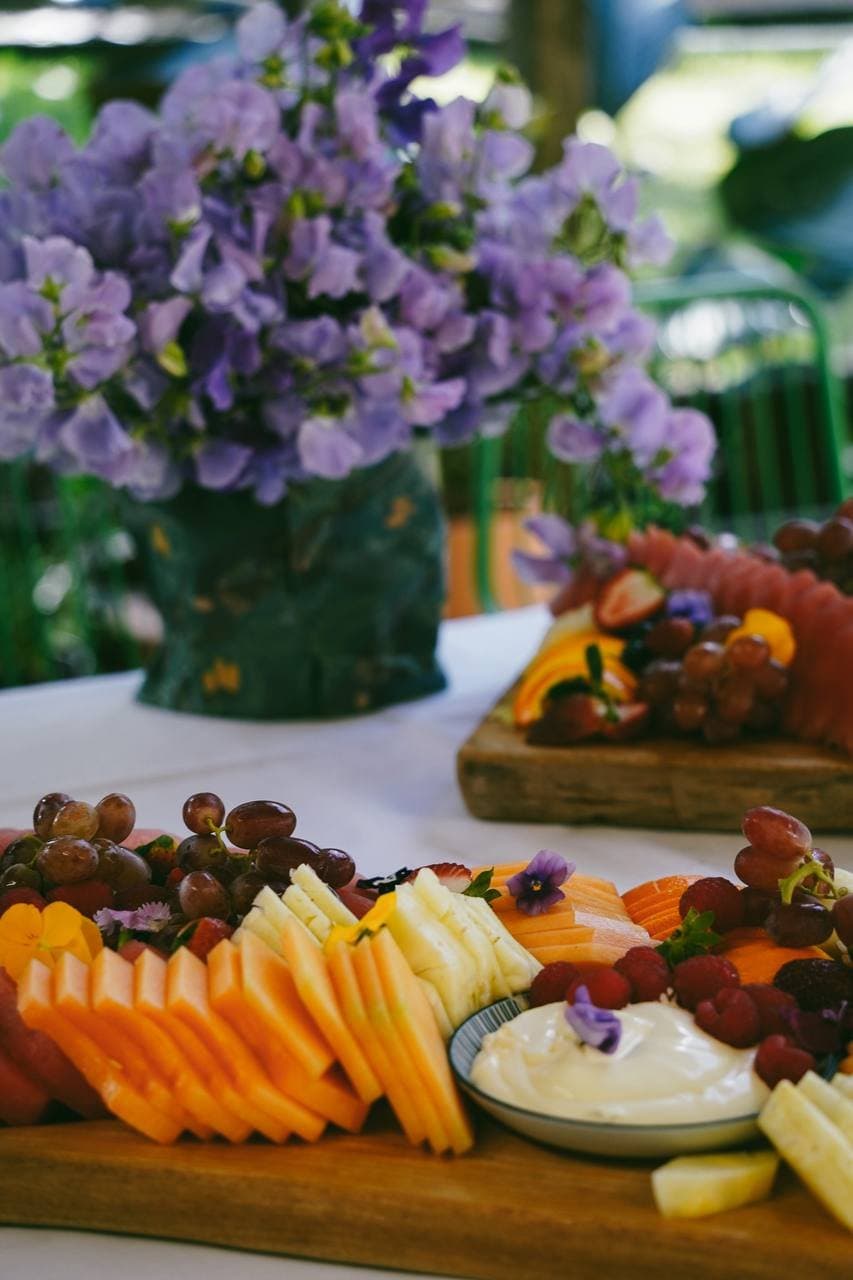 Seasonal fruit platter with edible flowers beside a vase of sweet peas at Fairhill