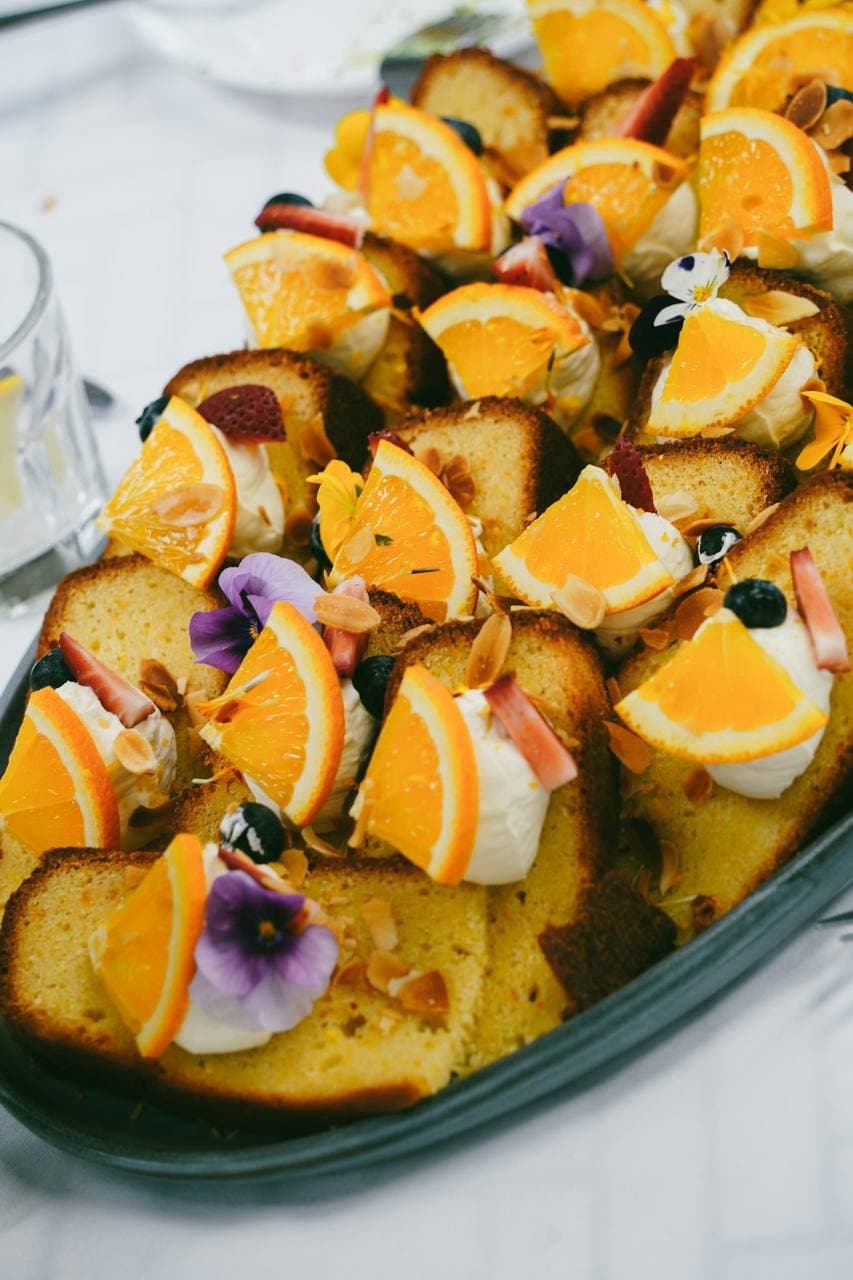 Platter of orange cake slices with cream, almonds and edible flowers
