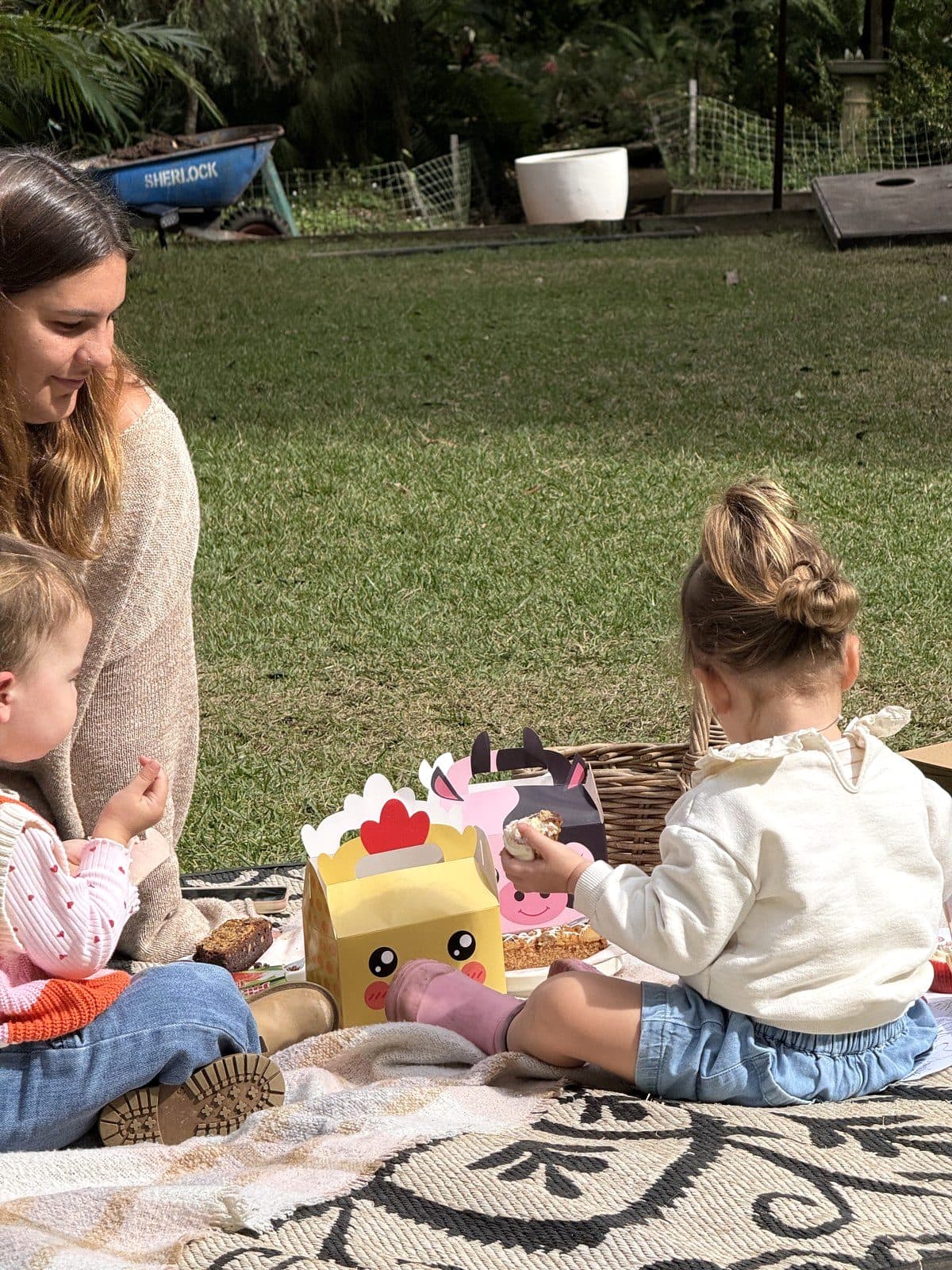 Toddlers sharing party cakes on a picnic rug in the gardens at Fairhill