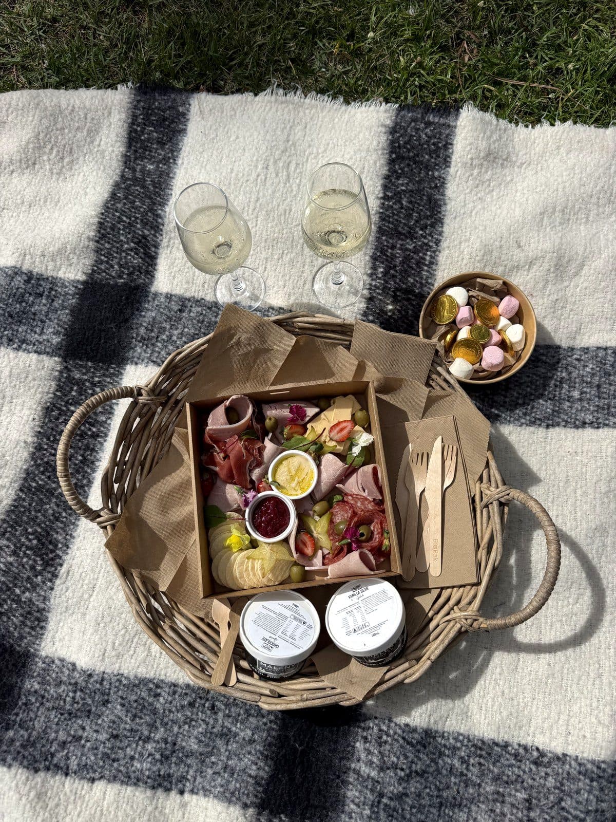 A grazing box picnic with two glasses of sparkling wine on a tartan rug at Fairhill