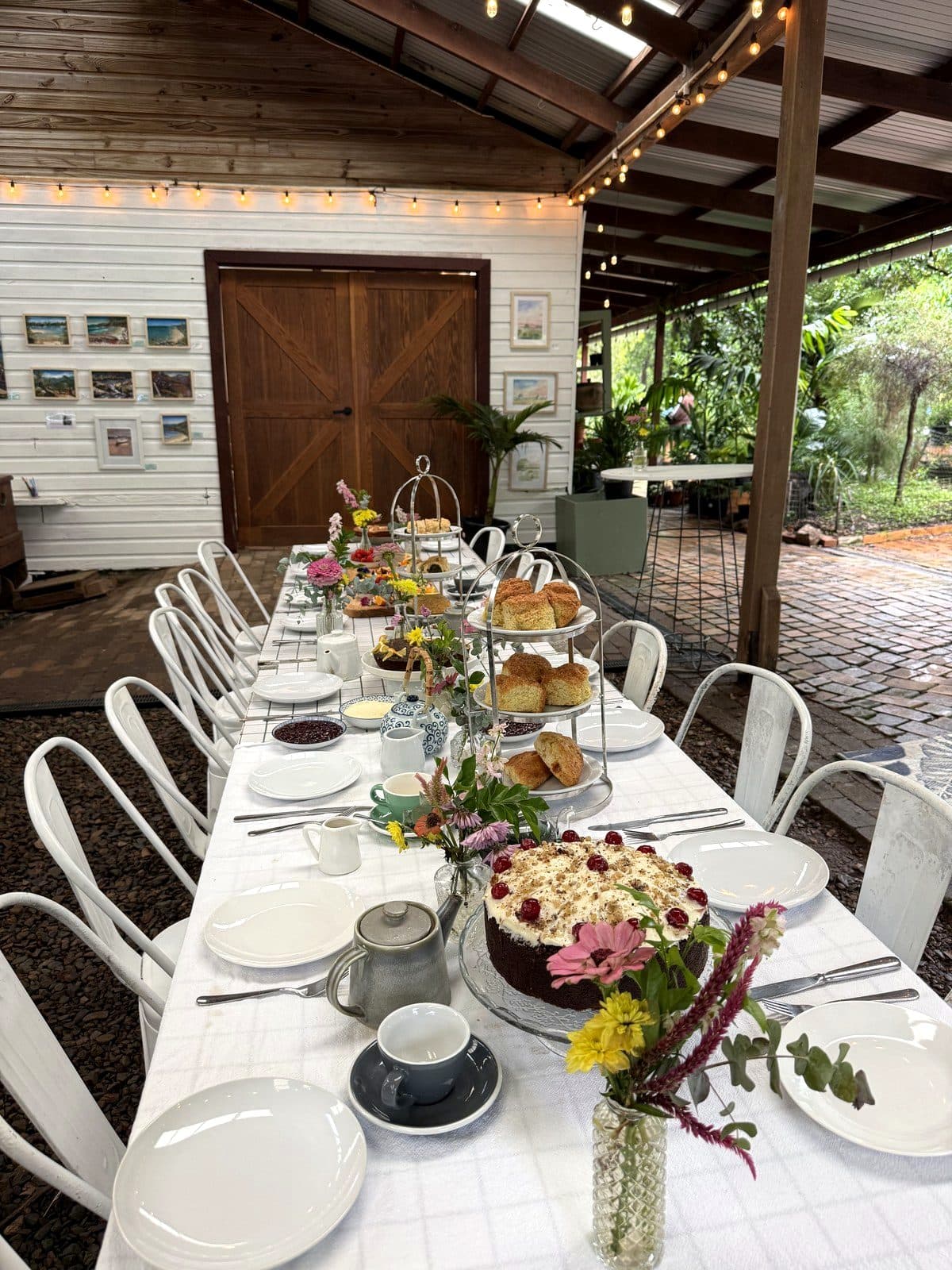 The Bush Harvest Morning Tea long table under fairy lights in the Fairhill pavilion, set with tiered scone stands, cake and fresh flowers