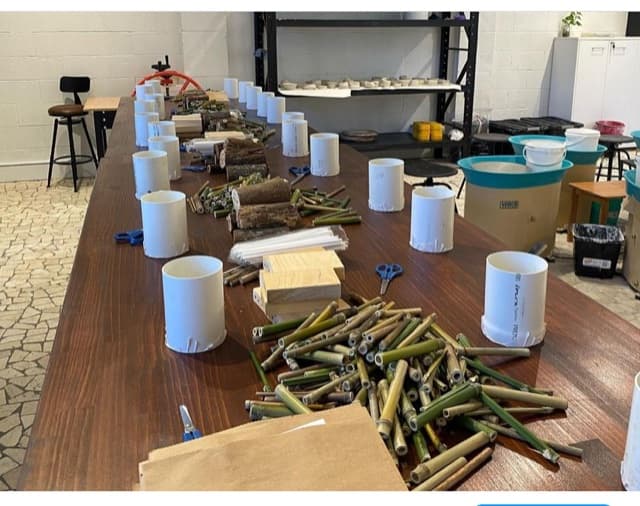 Bee hotel building stations set up along a workshop table, with bamboo tubes and materials at each place