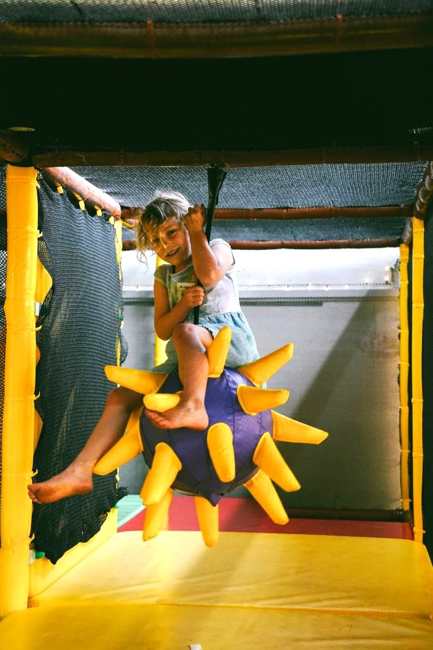 A young visitor swinging on the giant spike-ball swing inside Little Sprouts at Fairhill Adventure Gardens