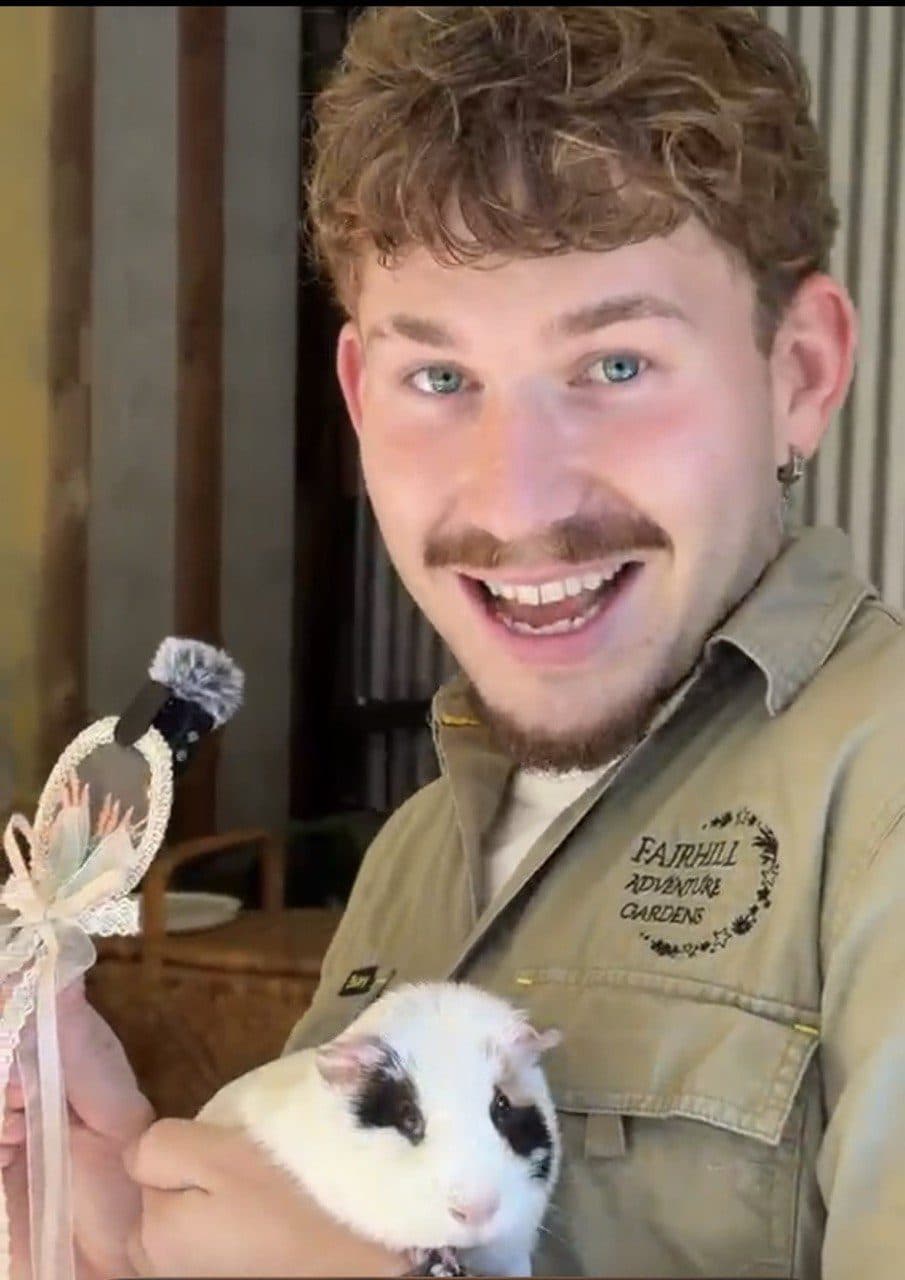 A smiling Fairhill Ranger holding a guinea pig during the Animal Farmyard Adventures