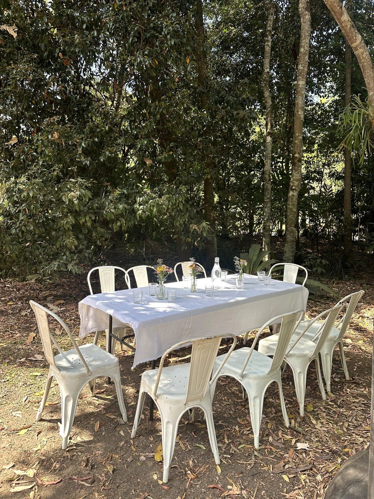 Ten place settings with garden posies on a long white table in the Fairhill forest